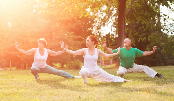 Two women and a man do yoga outdoors.